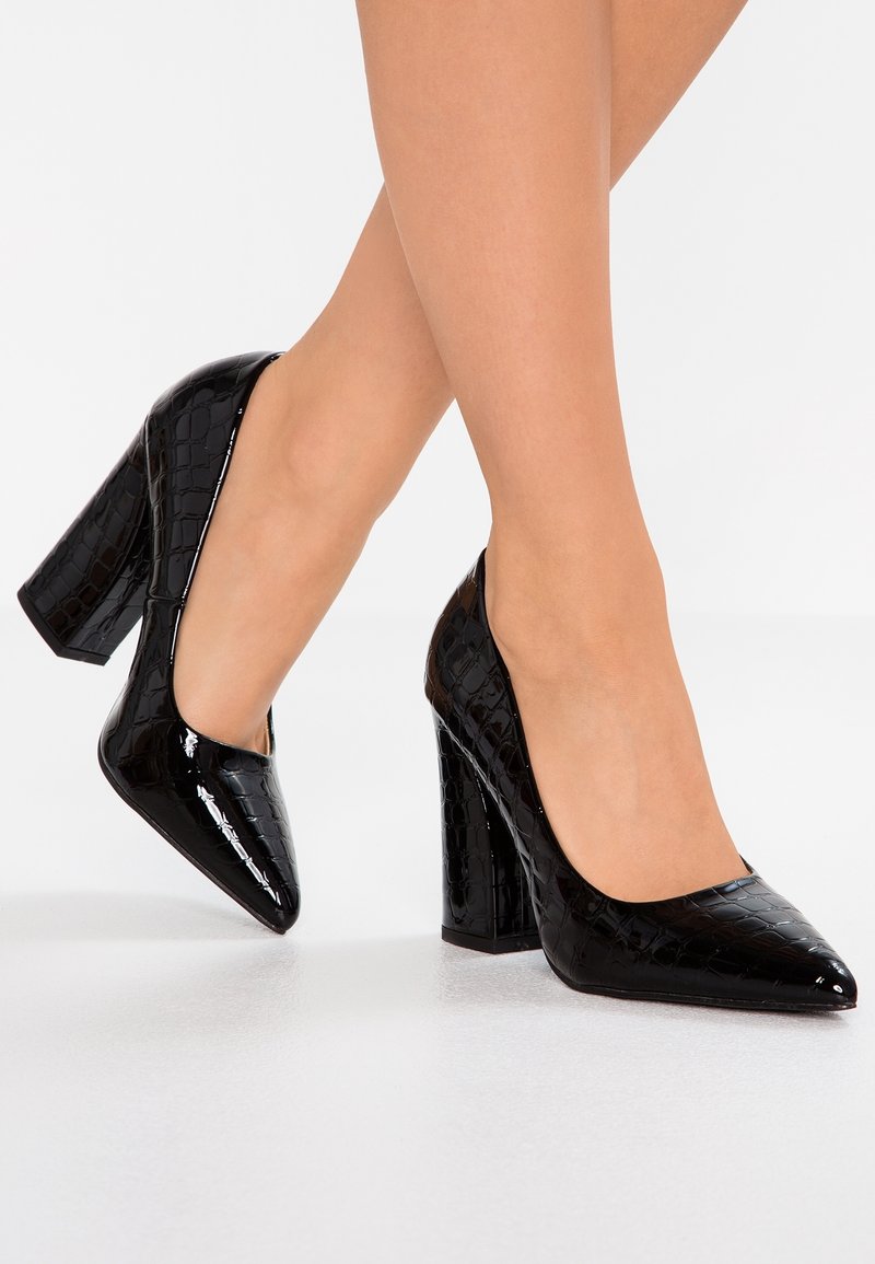 Escarpins en cuir verni noir à talons hauts avec une texture crocodile, bout pointu et talon épais, présentant un design épuré.