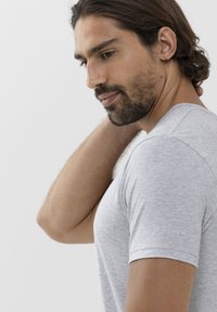 Grå kortärmad t-shirt med en mjuk struktur, figursydd design och subtilt melerat mönster, bärs av en man med axellångt hår.