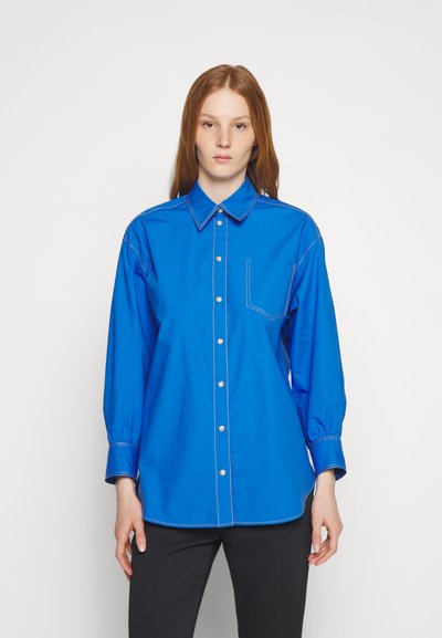 Γαλάζιο πουκάμισο με γιακά, που διαθέτει τσέπη στο στήθος, μακριά μανίκια και αντίθετη ραφή. Φτιαγμένο από λείο, ελαφρύ ύφασμα.