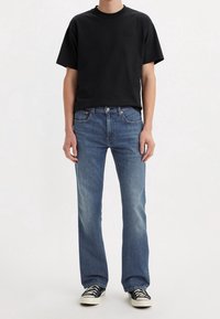 Camiseta negra de manga corta con logo en relieve, combinada con vaqueros de pierna ancha azul claro y zapatillas con patrón en blanco y negro.