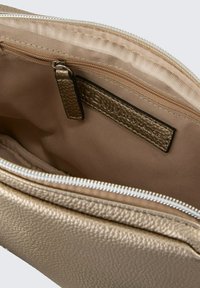 Innenraum der goldtexturierten Ledertasche mit einem cremefarbenen Futter. Verfügt über eine Reißverschlusstasche und ein Etikett. Überall glattes, strapazierfähiges Material.
