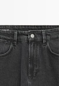 Czarne dżinsy o klasycznym kroju, z zapięciem na guzik, pięcioma kieszeniami i subtelną teksturą w jodełkę. Metka widoczna wewnątrz.