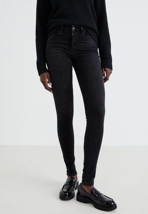 Black skinny jeans made of denim, featuring a fitted design, waistband with a button, and classic five-pocket styling, paired with black loafers.