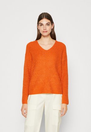 Orange Pullover mit V-Ausschnitt, langen Ärmeln und strukturiertem Muster sowie geripptem Saum, kombiniert mit creamfarbenen Weitbein-Hosen.