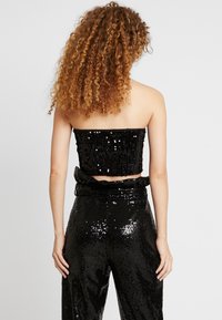 Černý top bez ramínek se flitry a zkráceným designem, kombinovaný s černými kalhotami s vysokým pasem a flitry, které mají nařasený pas.