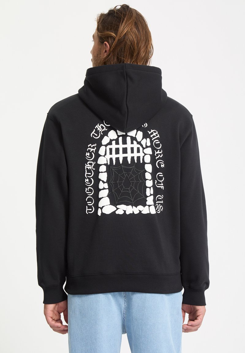 Sweat-shirt à capuche noir avec un grand graphisme blanc représentant une arche en pierre avec une toile d'araignée et du texte au dos. Matière en coton.