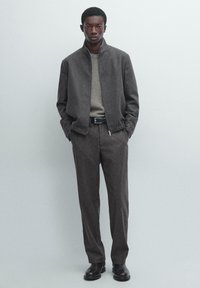 Grau melierte Wolljacke mit Reißverschluss, hellgrauer Pullover, maßgeschneiderte graue Hose, schwarzer Gürtel und schwarze Schuhe. Schlichtes Design mit glatter Textur.