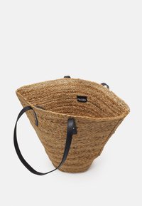 Woven straw tote bag with a conical shape, tan color, black faux leather handles, and interior label. Features a textured surface.