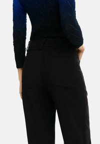 Pantalones negros con cintura ajustada y dos bolsillos traseros. La tela parece suave con un ligero brillo. Los detalles incluyen costuras visibles.
