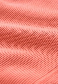 Audums ar ribveida rakstu, spilgtā korāļa krāsā, ar mīkstu tekstūru un redzamām šuvju detaļām, radot plūstošu izskatu.