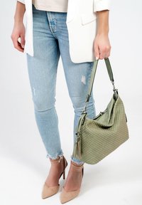 Zielona pleciona torebka o teksturowej powierzchni i pojedynczym pasku. W połączeniu z jasnoniebieskimi przetartymi dżinsami i cielistymi szpilkami.