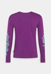 Pitkähihaisen purppuranpunaista t-paitaa, jossa on turkoosi lohikäärme ja kukkagrafiikat molemmissa hihoissa. Paita on valmistettu pehmeästä kankaasta, jossa on sileä tekstuuri.