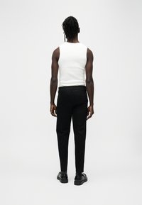 Débardeur blanc sans manches et pantalon noir à coupe ajustée, associés à des chaussures noires. Vue de dos, texture lisse et couleurs neutres.