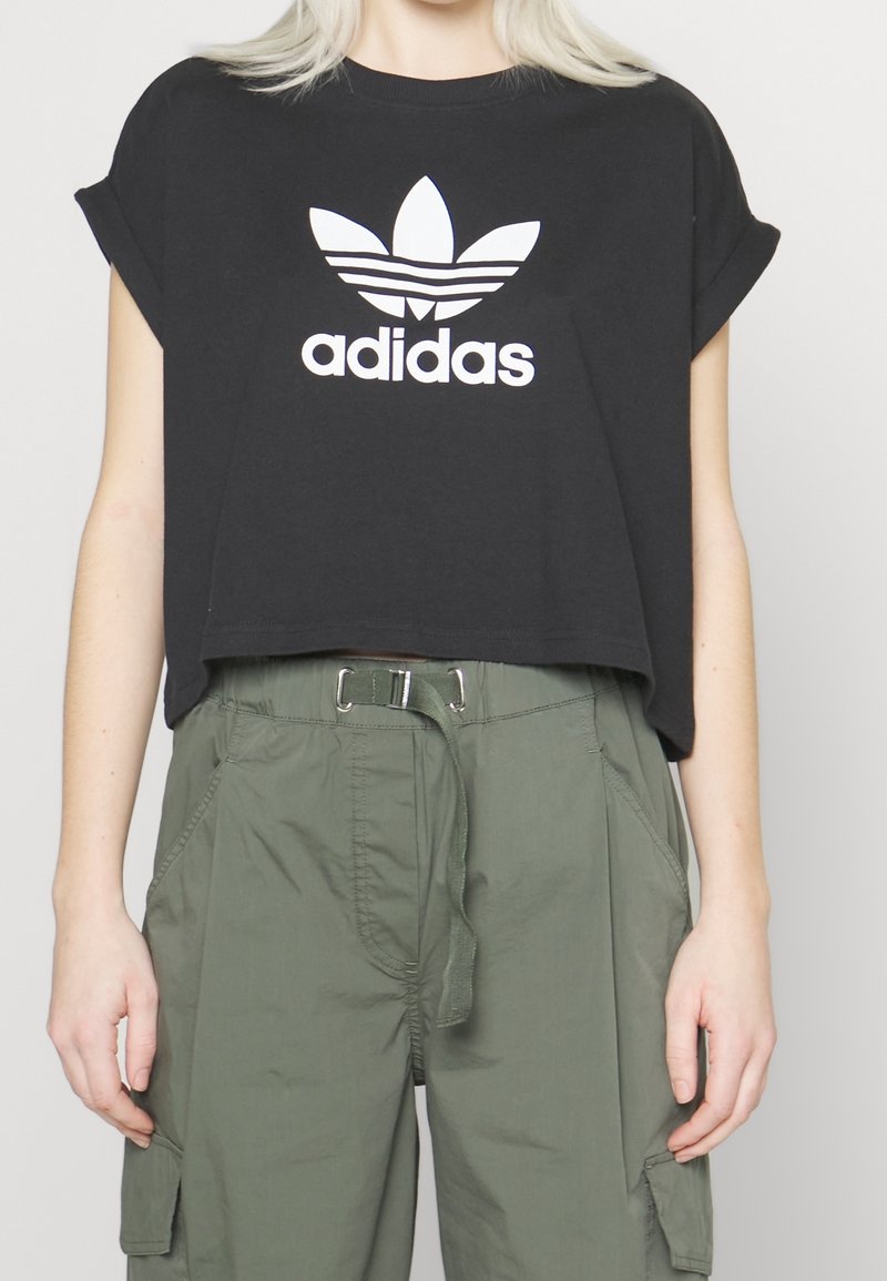 Person wearing a black cropped Adidas T-shirt and high-waisted olive green cargo pants with a fabric belt.