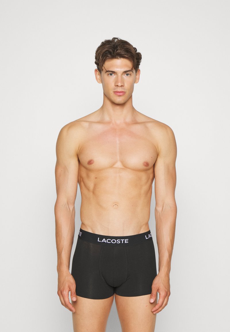 Black cotton boxer briefs with a stretchy waistband featuring the "Lacoste" logo in white. Smooth texture, fitted design.