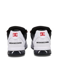 Vita och svarta sneakers med nätackenter, gummisulor och synlig luftdämpning. Röd logotyp på hälen och varumärke på sidan.