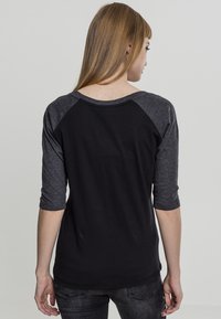 Svart og grå t-skjorte med trekvart ermer og rund hals. Mykt stoff, ribbestrikkede mansjetter og fargeblokkdesign på siden.
