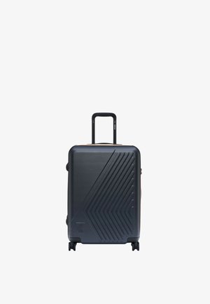 Czarna walizka twarda z ukośnymi wypukłymi liniami, cztery obrotowe kółka i wysunięta teleskopowa rączka na białym tle.