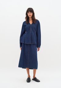 Denim kostüüm, kuhu kuulub pikakäiselise V-kaelusega peplum top ja sobiv pikk seelik. Tumedat sinist värvi, nähtavate õmbluste detailidega.