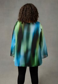 Blusa trasparente con una gradazione di colori blu, verde e nero. Vestibilità ampia con maniche a campana larghe. Tessuto morbido e design leggero.