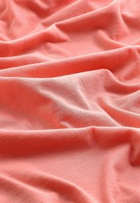 Tissu en corail doux avec une surface lisse et légèrement texturée, comportant des plis et des creux délicats qui créent de la profondeur et de la dimension.