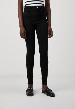 Høyt liv svarte skinny jeans med jevn tekstur, fem lommer og metallbeslag. Kombinert med svarte loafers med gullakenter.