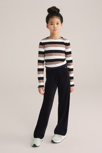 Ilgi piedurkņu svītrainā krekls brūnā, melnā un baltā krāsā; kombinēts ar platajiem melnajiem korduroja biksēm. Gaišas sporta apavas ar faktūru zoli.