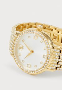 Gold watch with a round face, white dial, crystal hour markers, and a crystal-studded bezel; features a link bracelet design.