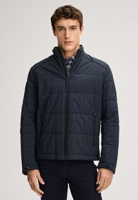 Granatowa kurtka puchowa z pikowanym wzorem, wysokim kołnierzem, zamkiem błyskawicznym z przodu i bocznymi kieszeniami. Miękka tekstura z minimalistycznym designem i akcentami guzików.