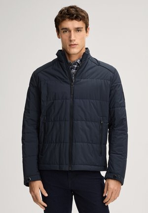 Marinefarbene Puffjacke mit gestepptem Muster, hohem Kragen, Frontreißverschluss und seitlichen Taschen. Weicher Stoff mit minimalistischem Design und Knopfakzenten.