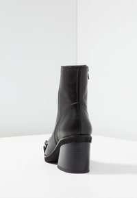 Bottine en cuir noir à bout arrondi, talon bloc et fermeture éclair à l'arrière. Une garniture argentée décorative orne le côté extérieur.