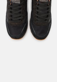 Paire de baskets noires avec des détails en mesh et en daim, lacets noirs et semelles en caoutchouc marron, vues de dessus sur fond blanc.