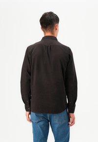 Camisa negra de manga larga con cuello abotonado, tela texturizada y puños de un solo botón, combinada con jeans de mezclilla azules.