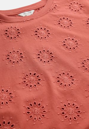 Lähikuva korallinvärisestä kankaasta, jossa on kirjailtuja kukkaisia läpikuultavia kuvioita ja pyöreä pääntie, jossa näkyy pieni vaatetunniste.