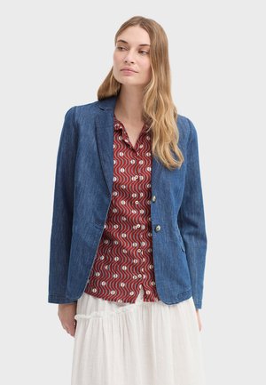 Donkerblauwe spijkerblazer met een getailleerde pasvorm, voorzien van een ingestikte reverskraag, twee knopen en voorzakken, gedragen over een rood overhemd met patroon.