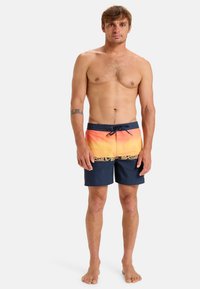 Simshorts med en gradient från orange till marinblå, snörning i midjan och stor stiliserad logotyp fram. Tillverkade av lätt tyg.