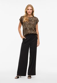 Haut à manches courtes imprimé léopard associé à un pantalon large noir. L'ensemble présente une coupe décontractée et un tissu texturé. Des sandales noires complètent le look.