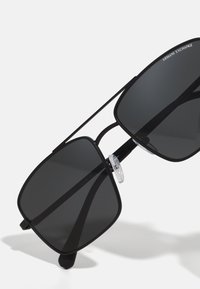 Ochelari de soare pătrați, negri, cu lentile închise, ramă din metal și suporturi pentru nas transparente. Design minimalist și formă elegantă. Accente la tâmple.