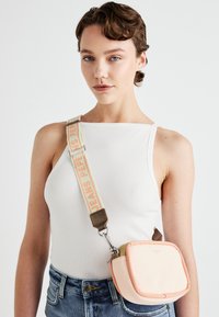 Lille rektangulær crossbody taske i blød lyserød med en tekstureret overflade, justerbar rem med "JEANS PEP" logo og sølvfarvede hardware detaljer.