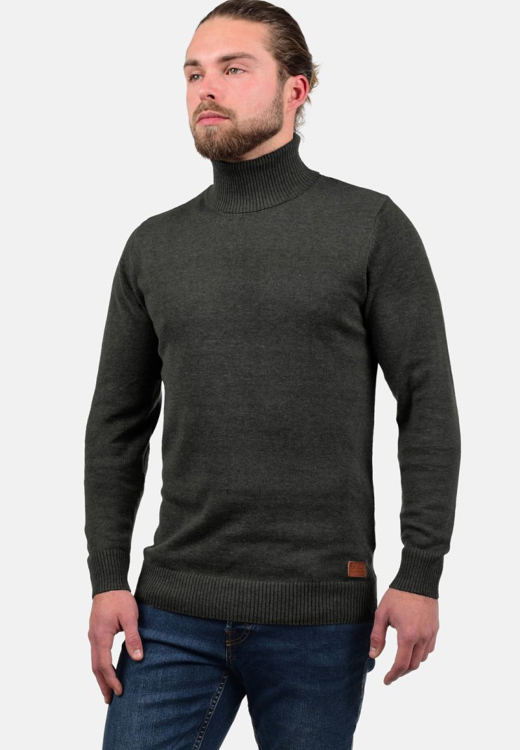 Tume roheline kõrge kaelusega särk, mis on valmistatud soonikust kootud kangast, pikaaegsete varrukatega ja nahast logopatchiga hemil. Kandnud koos siniste teksadega.