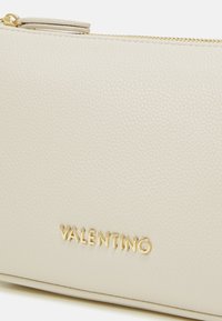 Kvačilo u mekoj bež koži s teksturiranim završetkom, s zlatnim zatvaračem i "Valentino" logotipom u zlatnom tisku.