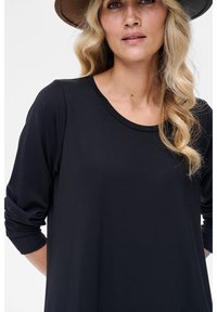 Czarna bluzka z długim rękawem i okrągłym dekoltem. Materiał jest gładki z lekkim połyskiem. Charakterystyczny marszczony detal na rękawach.