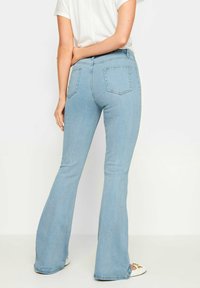 Ljusblå utsvängda jeans med hög midja, med bakfickor och en mjuk denimtextur, kombinerat med vita skor och en enkel t-shirt.