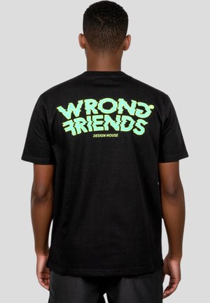 Black cotton t-shirt featuring bold, green graphic text "WRONG FRIENDS" on the back, with a rectangular logo underneath. Short sleeves.