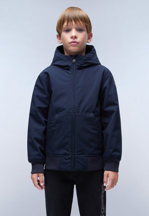Veste à capuche bleu marine en tissu lisse avec une fermeture éclair sur le devant et deux grandes poches. Elle possède des poignets côtelés et un emblème sur la manche.