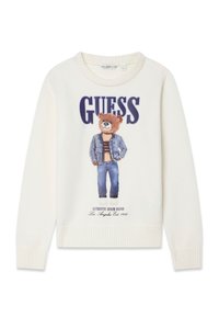 Pull blanc avec un imprimé d'ours portant une veste en jean et un jean, avec le texte « GUESS » au-dessus et des poignets et un ourlet côtelés.