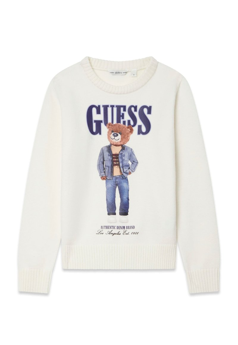 Pull blanc avec un imprimé d'ours portant une veste en jean et un jean, avec le texte « GUESS » au-dessus et des poignets et un ourlet côtelés.