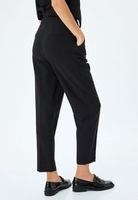 Zwarte tapered broek in een gladde stof, voorzien van zijzakken en een getailleerde pasvorm. In combinatie met glanzende zwarte loafers.