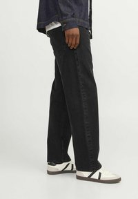 Vaqueros negros de pierna ancha con una textura suave y diseño clásico de cinco bolsillos, combinados con zapatillas blancas bajas con rayas negras.