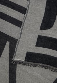 Grå og svart vevd stoff med bold geometriske mønstre og frynsete kant i nærbilde.